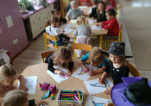 dzieci siedzą przy stolikach, kolorują obrazek z kapeluszem czarownicy