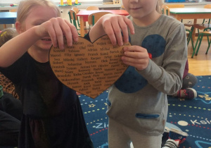 dwie dziewczynki przebijają papierowe serce z imionami
