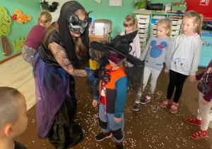dzieci stoją w kręgu, nauczycielka przebrana za czarownicę kręci jednym z chłopców, który ma opaskę na oczach