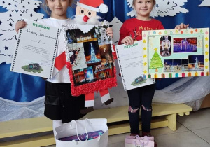 dwie dziwczynki prezentują swoje prace konkursowe oraz otrzymane nagrody i dyplomy