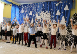 grupa odświetnie ubranych dzieci tańczy w szatni, wyrzucają w górę pocięte kartki imitujące śnieg