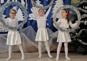 trzy dziewczynki przebrane za śnieżynki, w dłoniach mają koła ze srebrnymi łańcuchami na choinkę