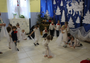grupa dzieci ubranych odświętnie tańczy z białymi chusteczkami, obok stoi nauczycielka