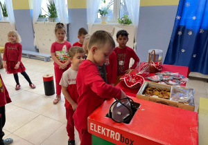dzieci ubrane na czerwono wrzucają do specjalnych pojemników zużyte baterie i elektrośmieci