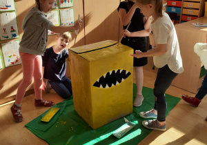 kilkoro dzieci maluje na żółto wielkie pudełko