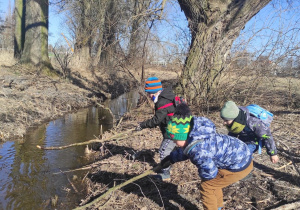 grupa dzieci nad brzegiem rzeki, w rękach mają kije