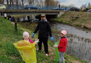 tata z córkami zbiera śmieci wzdłuż rzeki