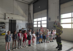 grupa dzieci w budynku straży słucha strażaka