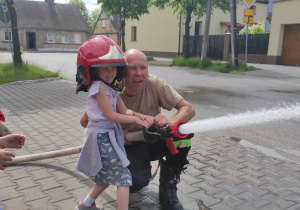 dziewczynka ze strażakiem leją wodę z węża