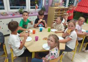 grupa dzieci przy stoliku je pizzę