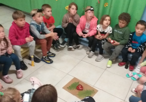 grupa dzieci w przedszkolnej szatni, siedzą w kręgu, słuchają opowieści o kwiecie paproci