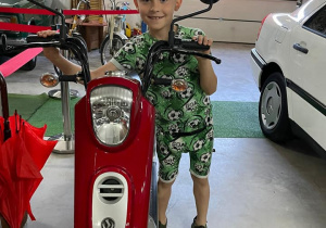 chłopiec pozuje do zdjęcia przy zabytkowym czerwonym motocyklu