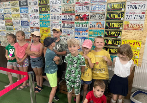 grupa dzieci stoi przy ścianie, na której są rejestracje stanów w USA