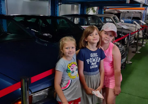troje dzieci pozuje do wspólnego zdjęcia przy zabytkowych autach