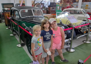 troje dzieci pozuje do wspólnego zdjęcia przy zabytkowych autach