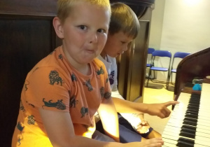 dwóch chłopców siedzi przy organach, naciskają klawisze, obok nich stoi pan od rytmiki