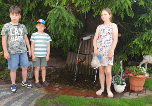 troje dzieci stoi przy studni artezyjskiej