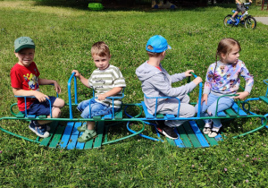 czworo dzieci w ogrodzie przedszkolnym siedzi na chuśtawkach