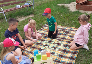 kilkoro dzieci siedzi na kocu w ogrodzie, grają w "segregację odpadów"
