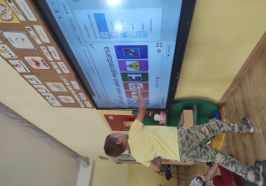 chłopiec w żółtej koszulce wykonuje zadanie przy tablicy multimedialnej