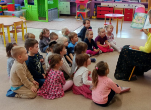 dzieci siedzą na dywanie, słuchają czytanego przez nauczycielkę opowiadania