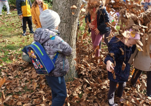 grupa dzieci bawi się podrzucając liście