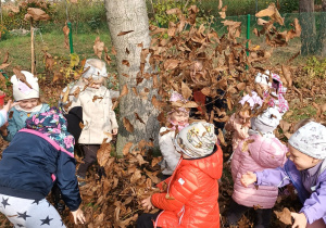 grupa dzieci bawi się przy drzewie podrzucając liście