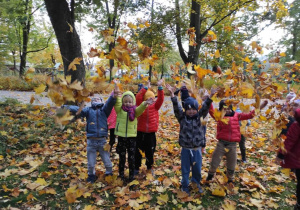 grupa dzieci bawi się e podrzucając liście