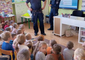 dzieci na krzesełkach w klasie, dwóch policjantów omawia zasady bezpieczeństwa