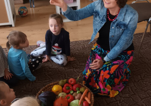 pani dietetyczka siedzi na dywanie i prezentuje kolorowe warzywa, obok niej dzieci