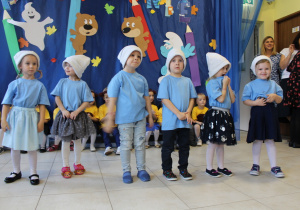 Grupa dzieci w strojach smerfów stoi przed publicznością i recytuje wiersz.