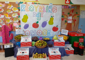 stoisko z owocami, w tle napis "Recykling daje owoce " i pudła na baterie i elektroodpady