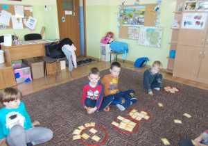 dzieci siedzą na dywanie obok nich plansze z literami