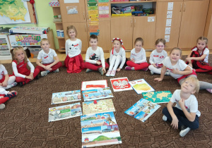 dzieci ubrane w biało-czerwone barwy siedzą na dywanie. przed nimi leżą karty z symbolami narodowymi, mapami