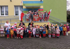 grupa dzieci i nauczycielki stoją przed budynkiem przedszkola, przygotowują się do uroczystego zaśpiewania Mazurka Dąbrowskiego
