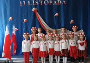 grupa dzieci pozuje do zdjęcia , w tle napis 11 listopada, wszystkie dzieci w białoczerwonych ubraniach, dziewczynki mają na głowach biało-czerwone wianki