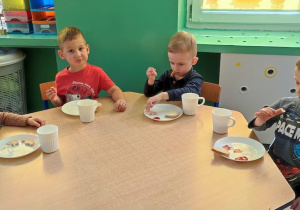 Grupa dzieci siedzi przy stoliku i zjada posiłek.