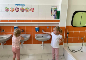 Dwie dziewczynki odkręcają kran i myją ręce.