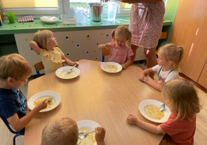 Grupa dzieci siedzi przy stoliku i zjada zupę.