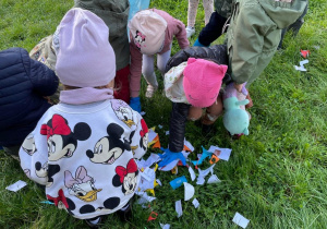 Dzieci zbierają śmieci rozrzucone w ogrodzie przedszkolnym.