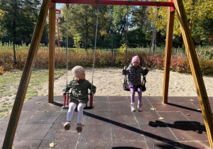 Dwie dziewczynki bujają się na huśtawkach w parku.