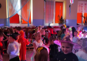 Dzieci tańczą w parach podczas przedszkolnego balu. Mają na sobie stroje karnawałowe.