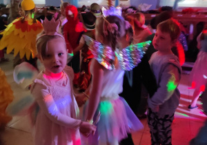 Dzieci tańczą w parach podczas przedszkolnego balu. Mają na sobie stroje karnawałowe.
