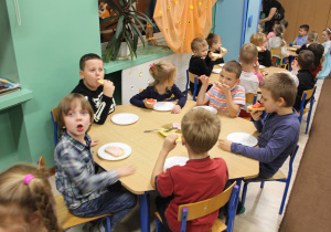 grupa dzieci je kolację przy stolikach