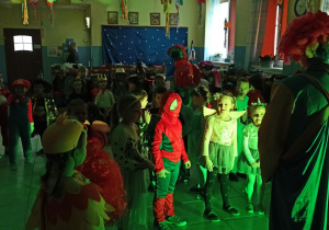 Dzieci przebrane w różne postaci, tańczą w przedszkolnej szatni, obok nich DJ prowadzący zabawę przebrany za klauna