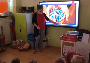 nauczycielka przy tablicy multimedialnej prowadzi zajęcia edukacyjne , na dywanie siedzą dzieci