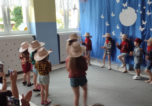 grupa dziewczynek ubranych w koszule w kratkę i kowbojskie kapelusze tańczy "swing w uliczce"