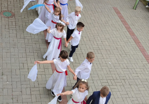 grupa dzieci tańczy walca , dziewczynki w białych sukienkach, chłopcy ubrani na galowo