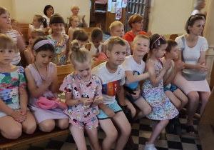 dzieci i nauczycielki siedzą w kościelnych ławach , słuchają koncertu