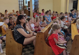 dzieci i nauczycielki siedzą w kościelnych ławach , słuchają koncertu